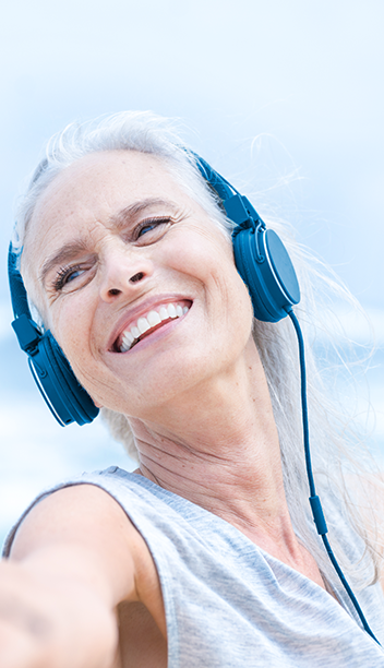 Woman in tank top with ear phones stretching her arm out. She is by the sea.